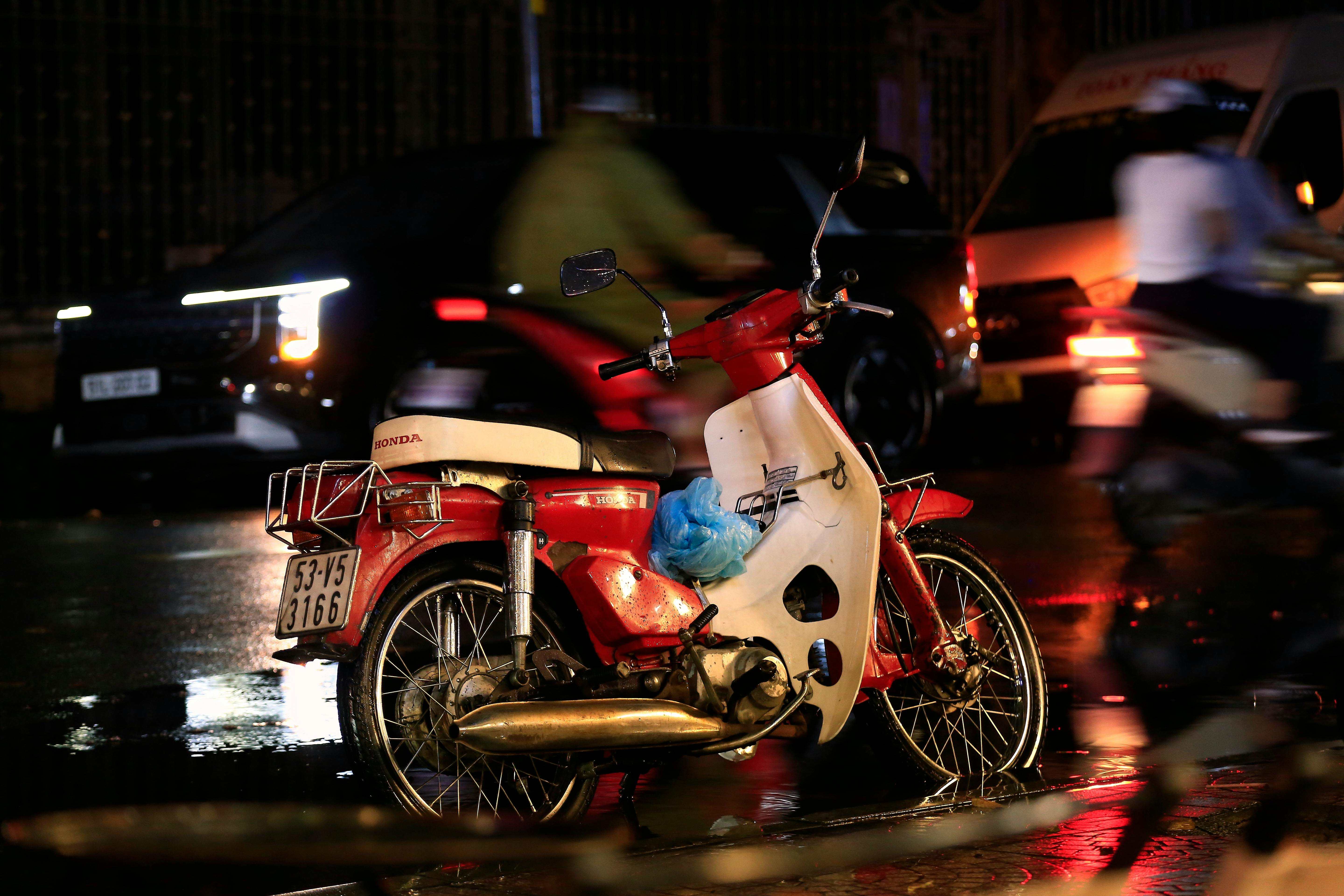 A vintage Honda motorcycle parked on a wet street at night in Ho Chi Minh City.