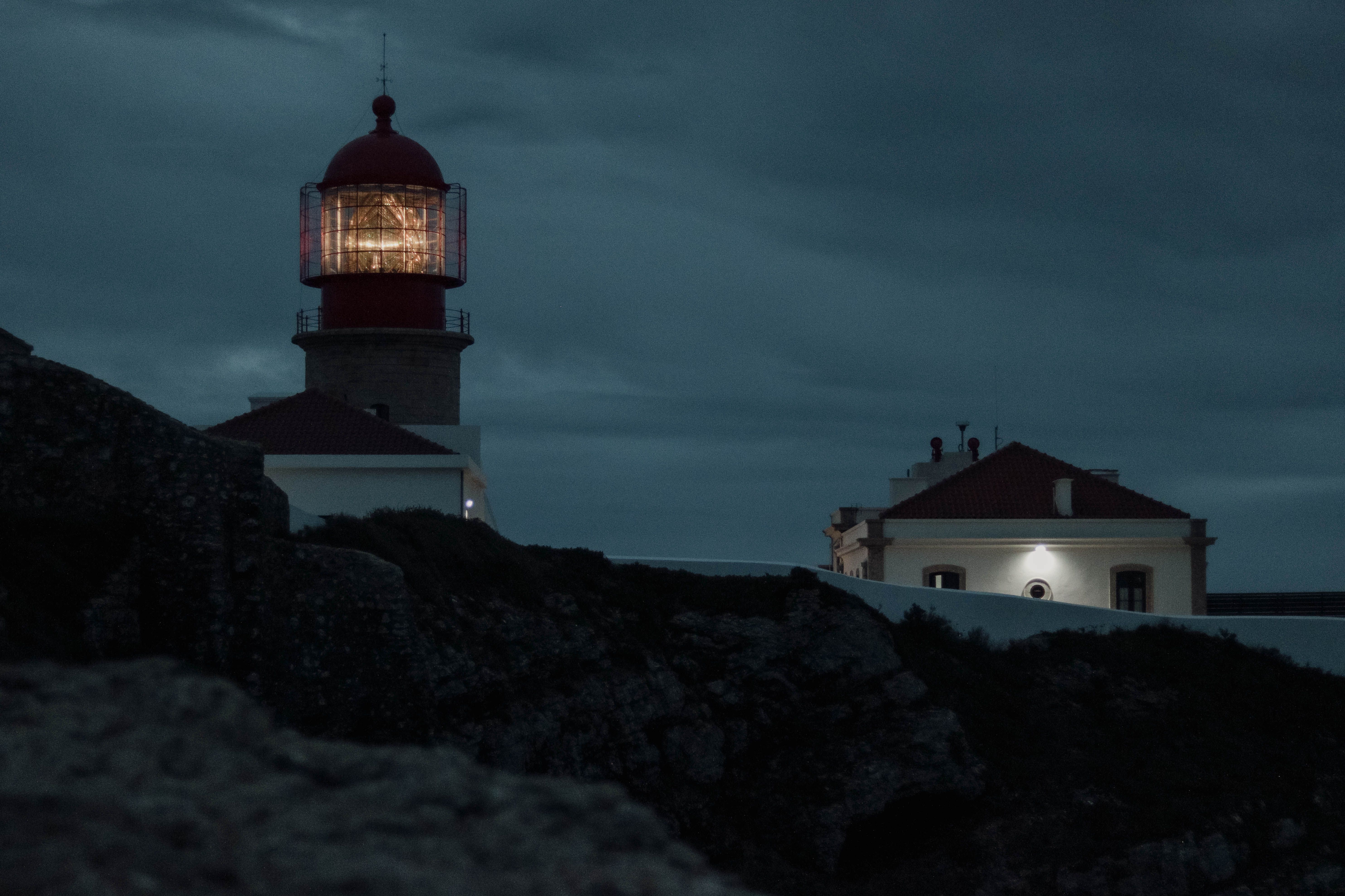 Illuminated Lighthouse at Dusk on Rocky Coastline · Free Stock Photo