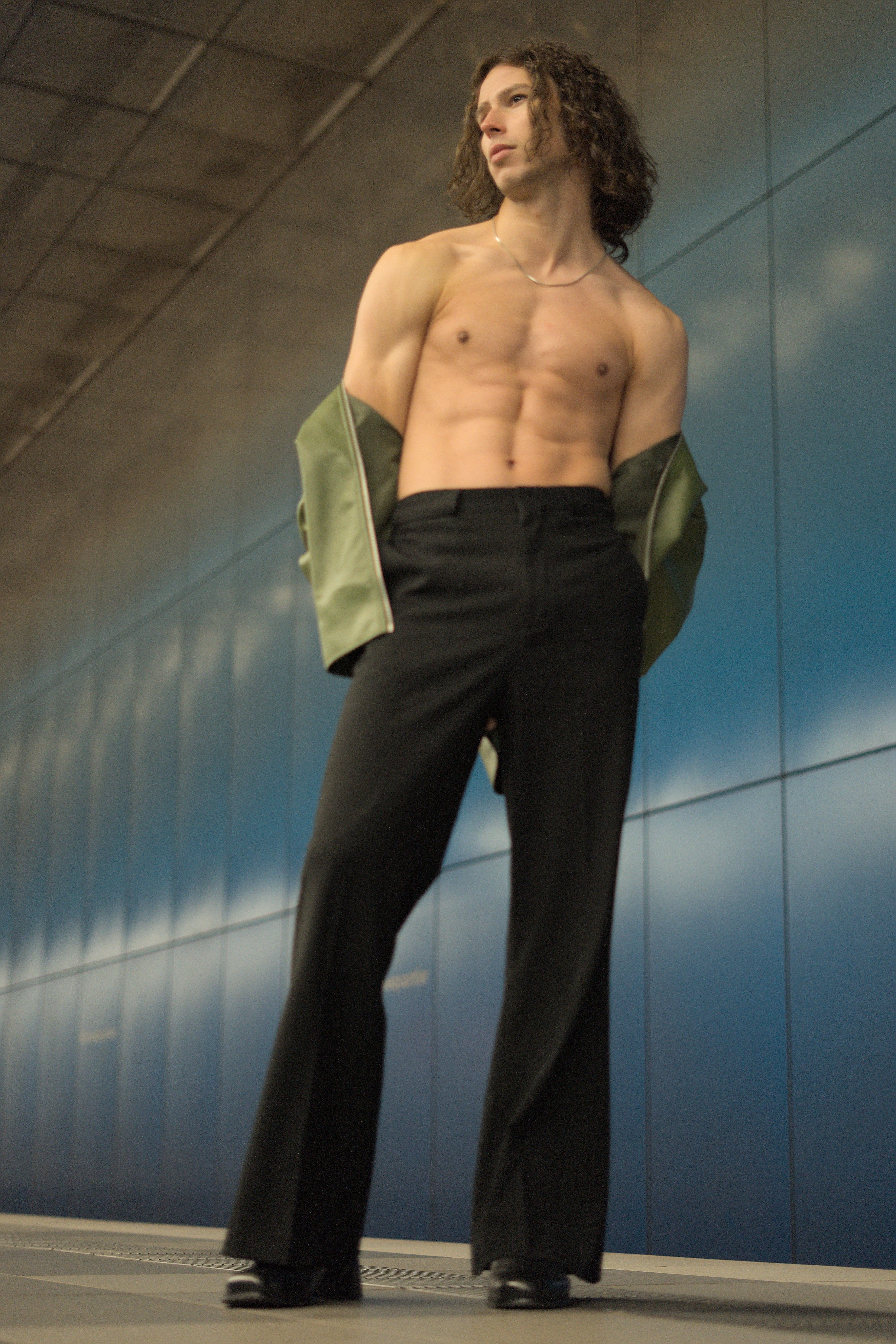 Young male model posing shirtless with a jacket in an urban environment. Fashion-forward and confident.
