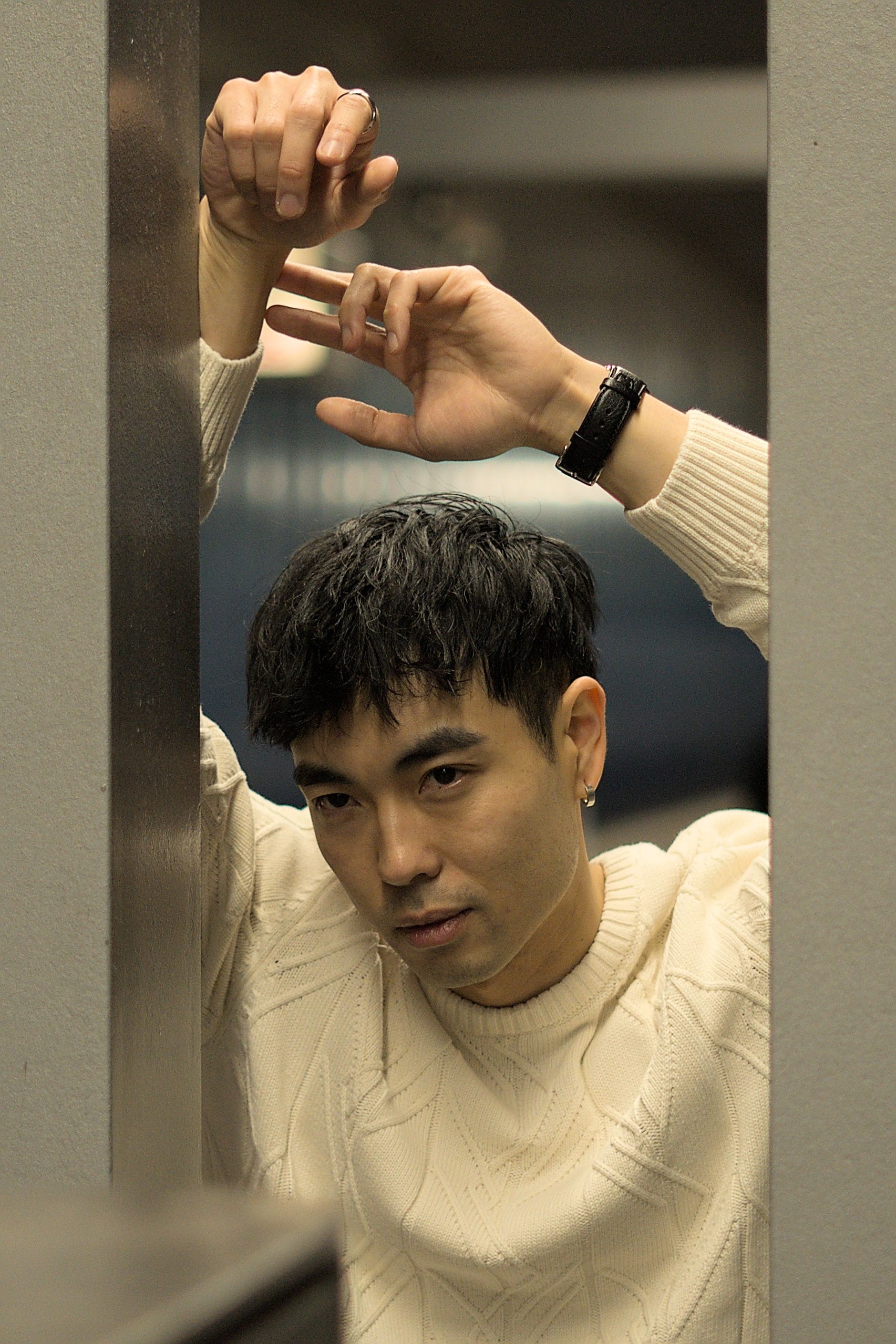 A young man in a white sweater leans against a wall, looking pensive.