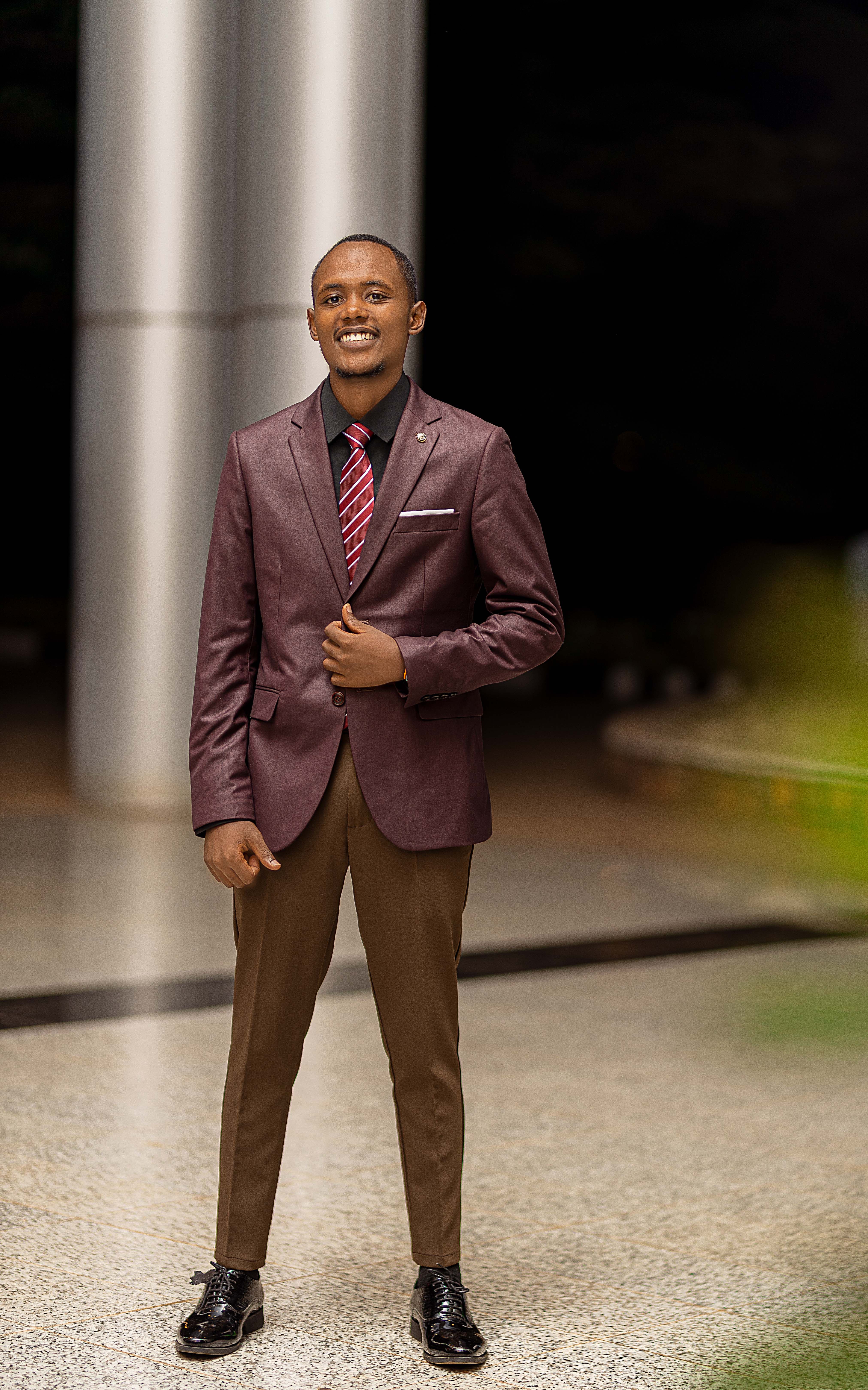Young man in maroon suit posing confidently outside at night.