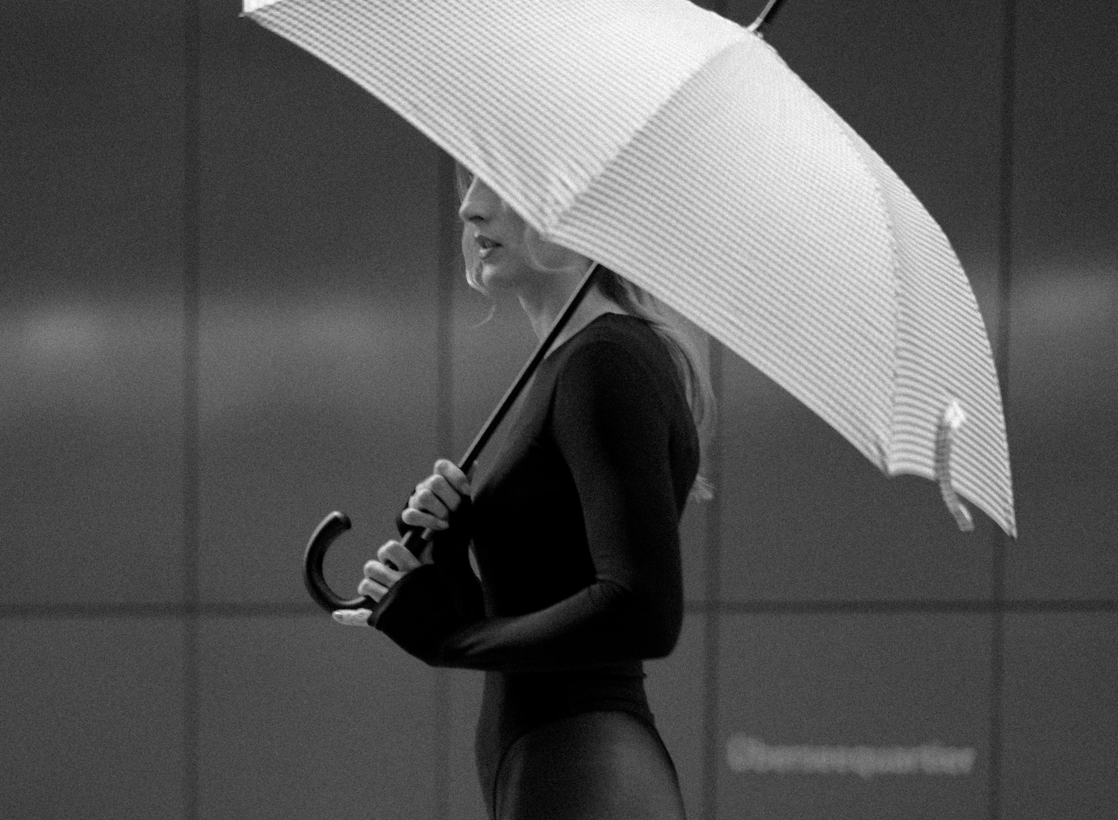 A person holding a high-quality, stylish umbrella with a wooden handle, confidently walking through a rain-soaked city street, embodying sustainable fashion.