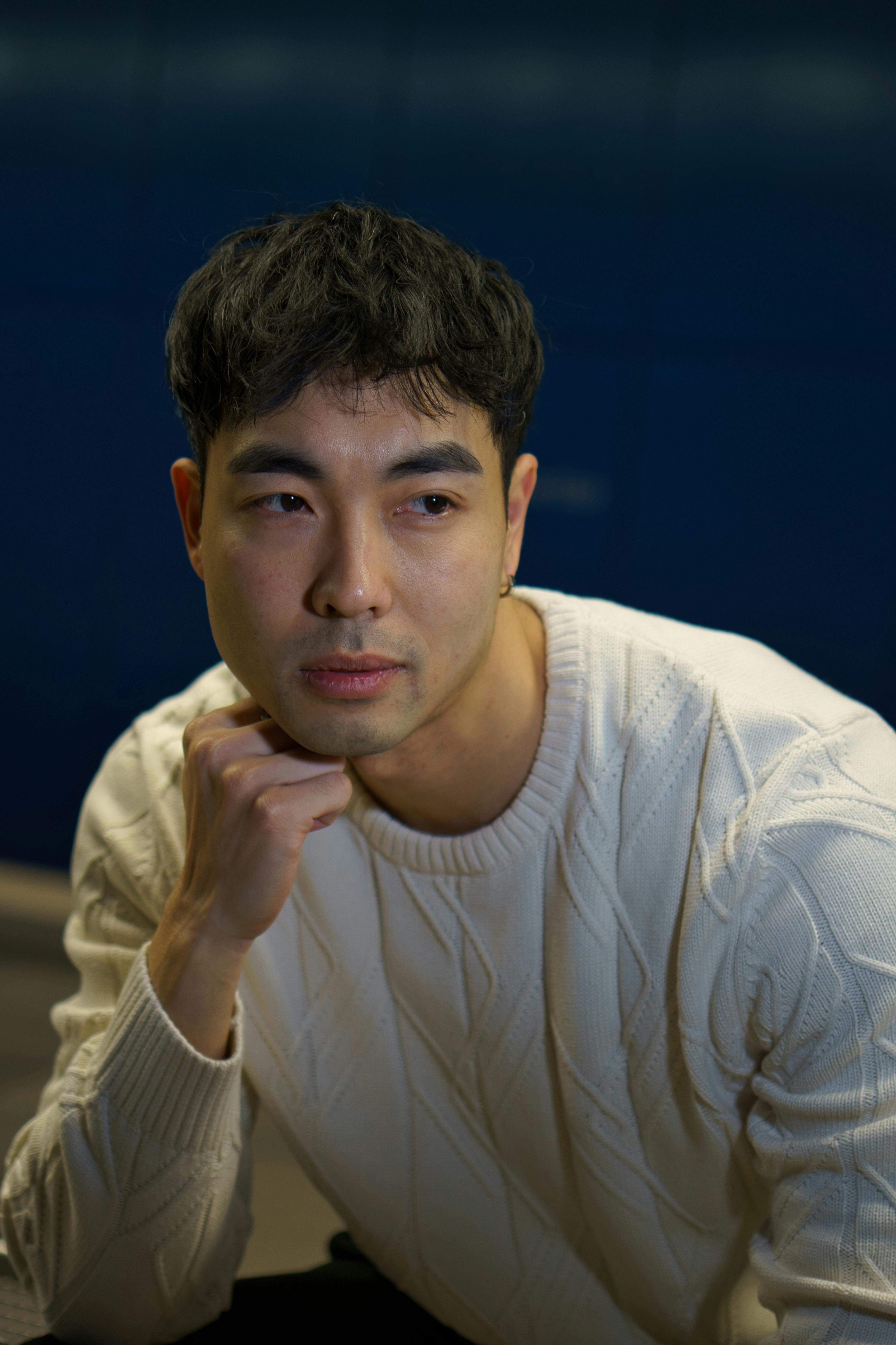 Portrait of a thoughtful young man in a white sweater against a blue background indoors.