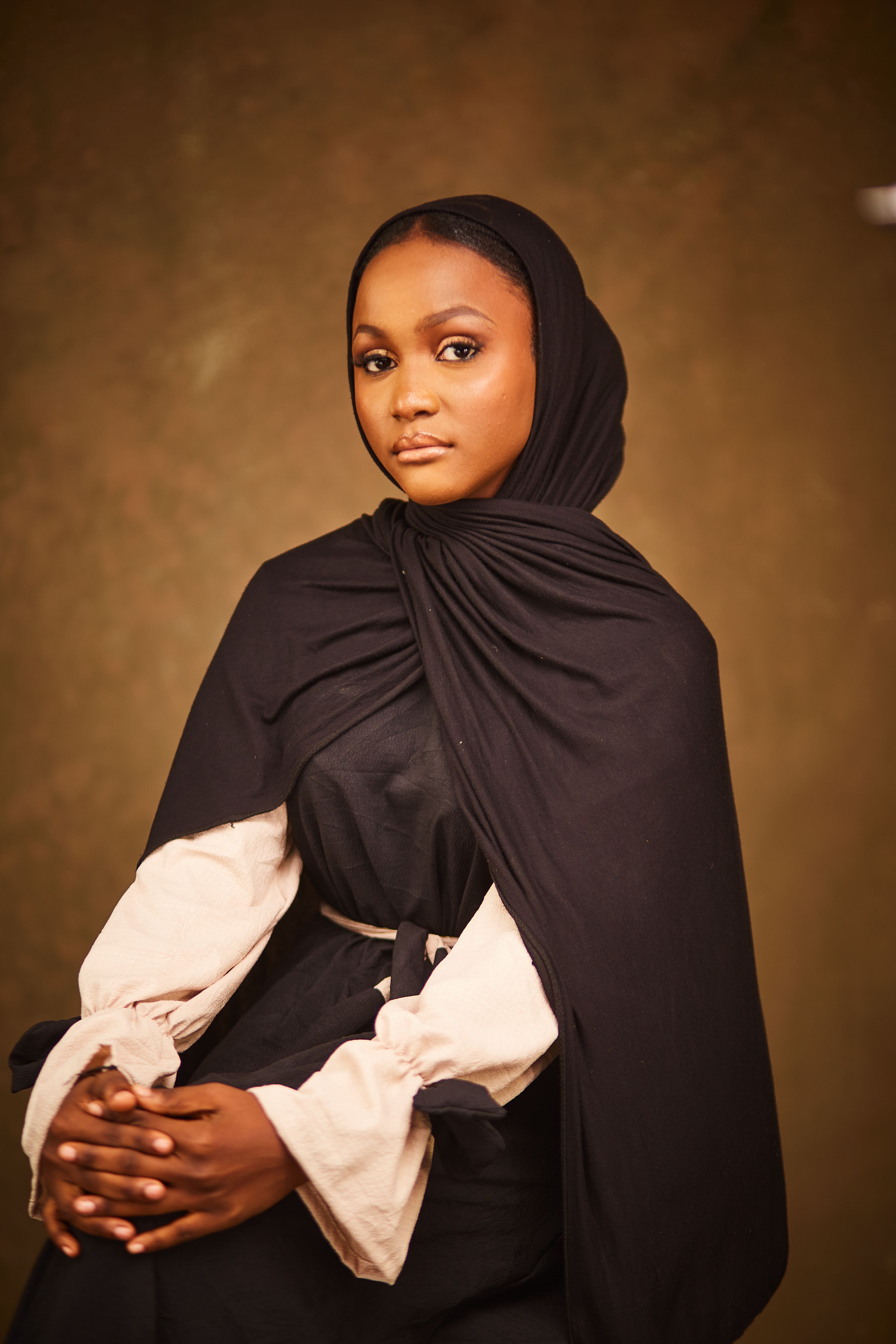 Elegant portrait of a woman wearing a traditional black hijab and robe with a neutral background.