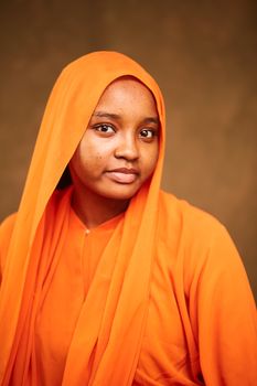 Close-up portrait of a woman wearing an orange hijab against a warm background.