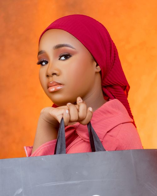 Free Portrait of a young woman in a red hijab, holding a shopping bag, set against a warm background. Stock Photo
