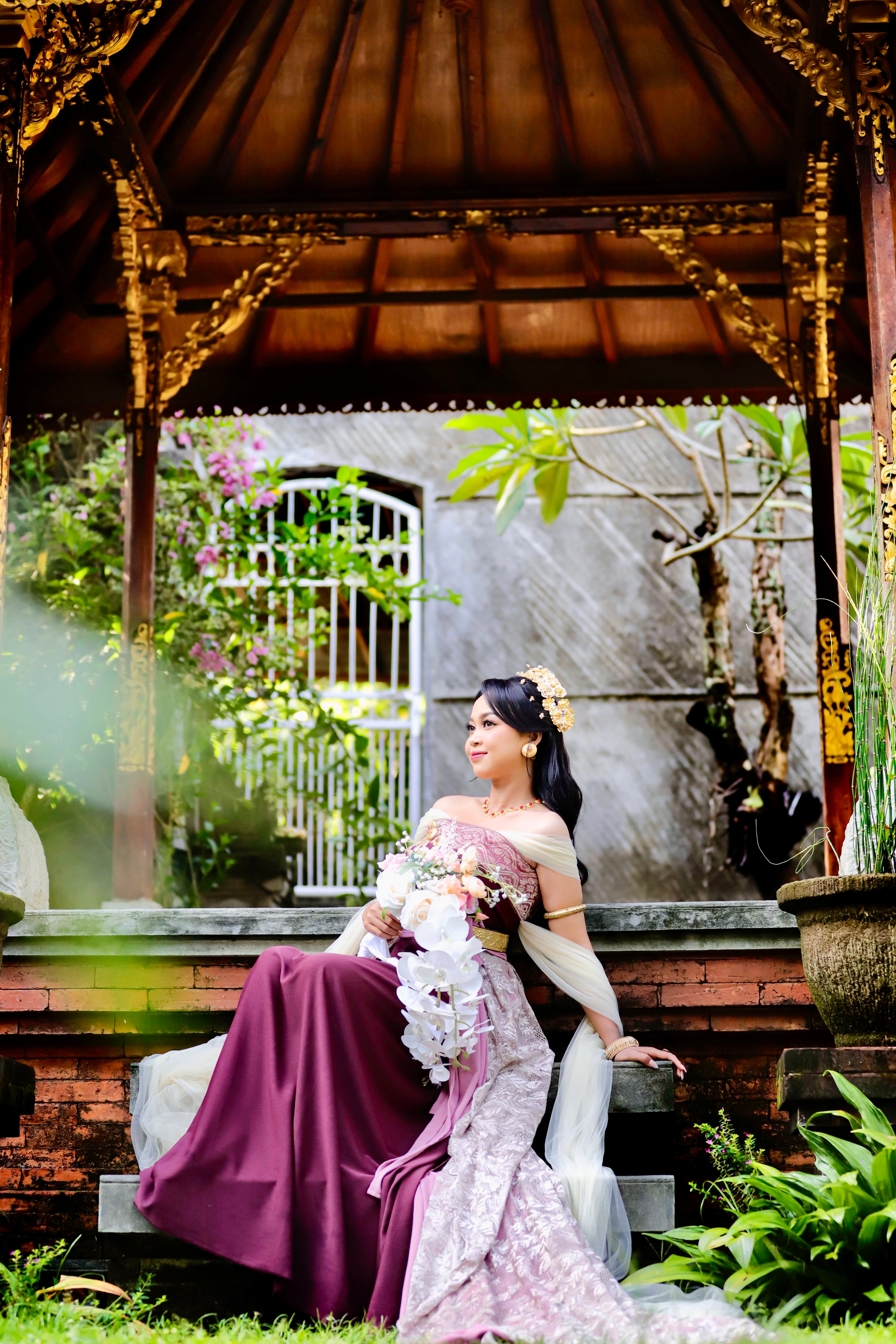 A woman in traditional attire sits gracefully in a Balinese-style pavilion in Nusa Tenggara Barat, Indonesia.