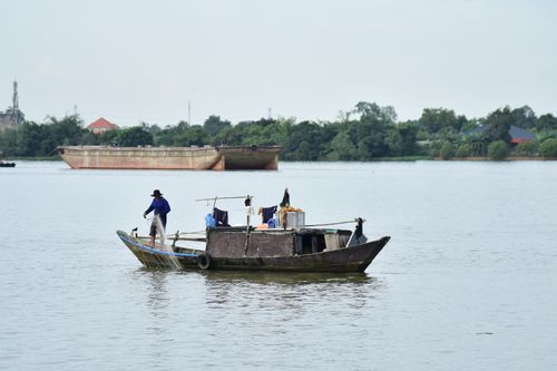 Free A lone fisherman on a traditional wooden boat navigates calm river waters. Stock Photo