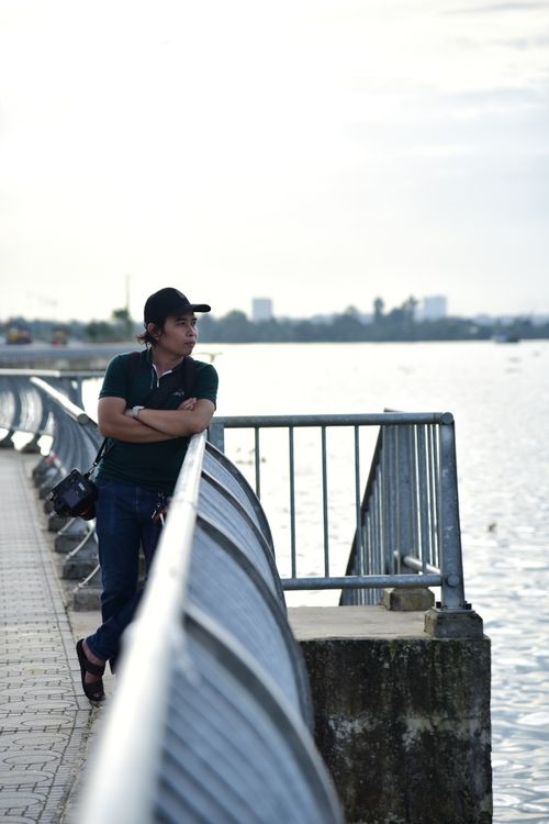 Free Man leaning on a railing by the water, enjoying a calm waterfront view during the day. Stock Photo