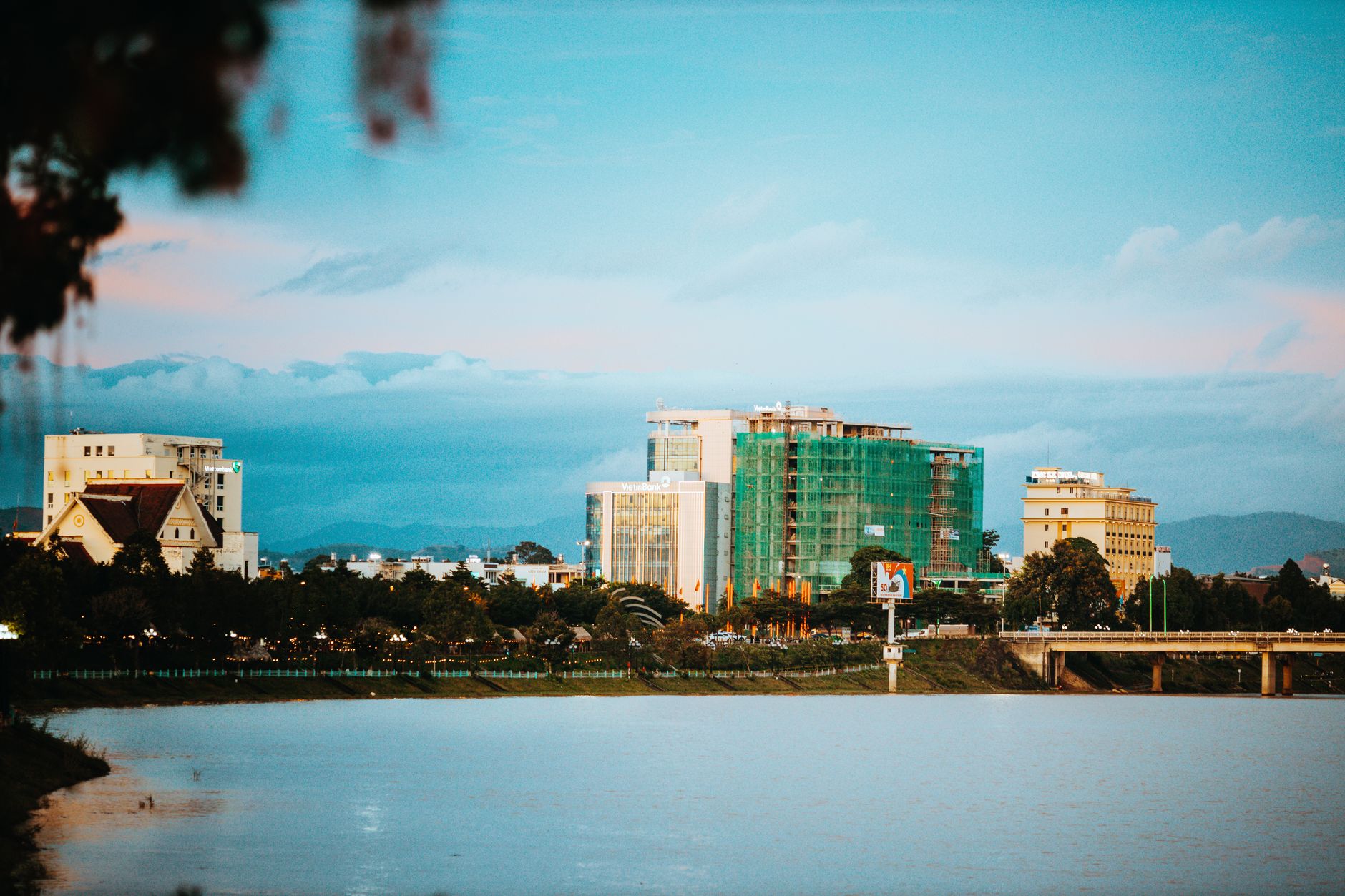 Peaceful view of Kon Tum's skyline reflecting over water at dusk with clouds visible.
