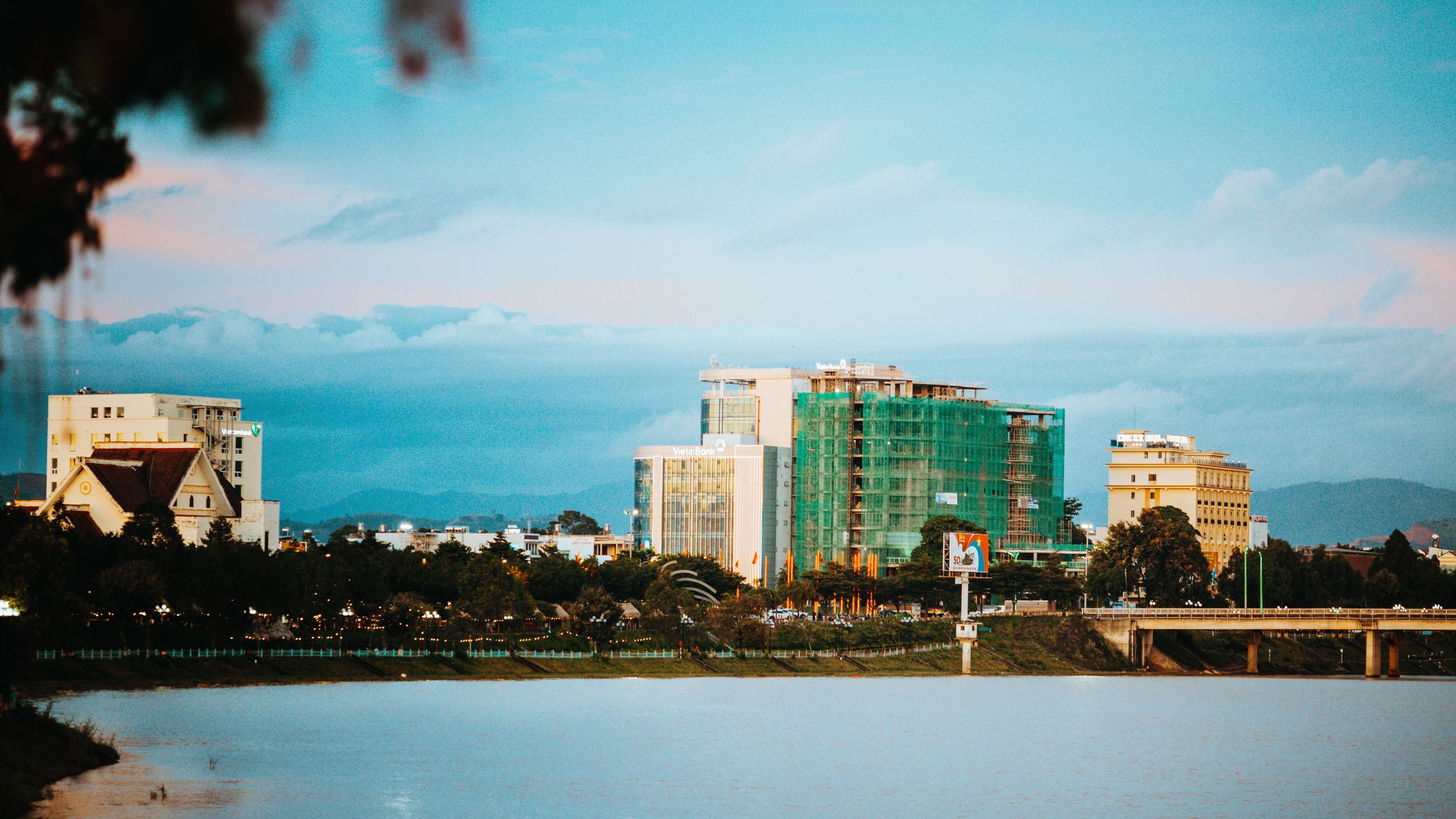 Peaceful view of Kon Tum's skyline reflecting over water at dusk with clouds visible.