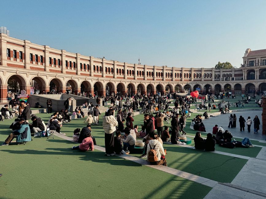 A bustling day at an Italian-style plaza filled with people enjoying outdoor leisure activities under the clear sky.
