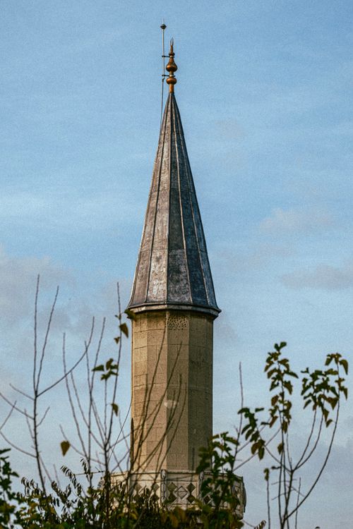 Free A classic architectural spire set against a clear blue sky, surrounded by lush foliage. Stock Photo
