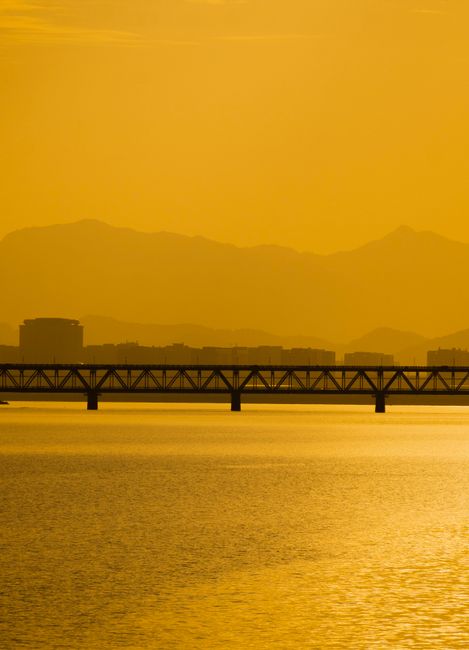 A tranquil scene of a bridge silhouetted against golden mountains at sunset.