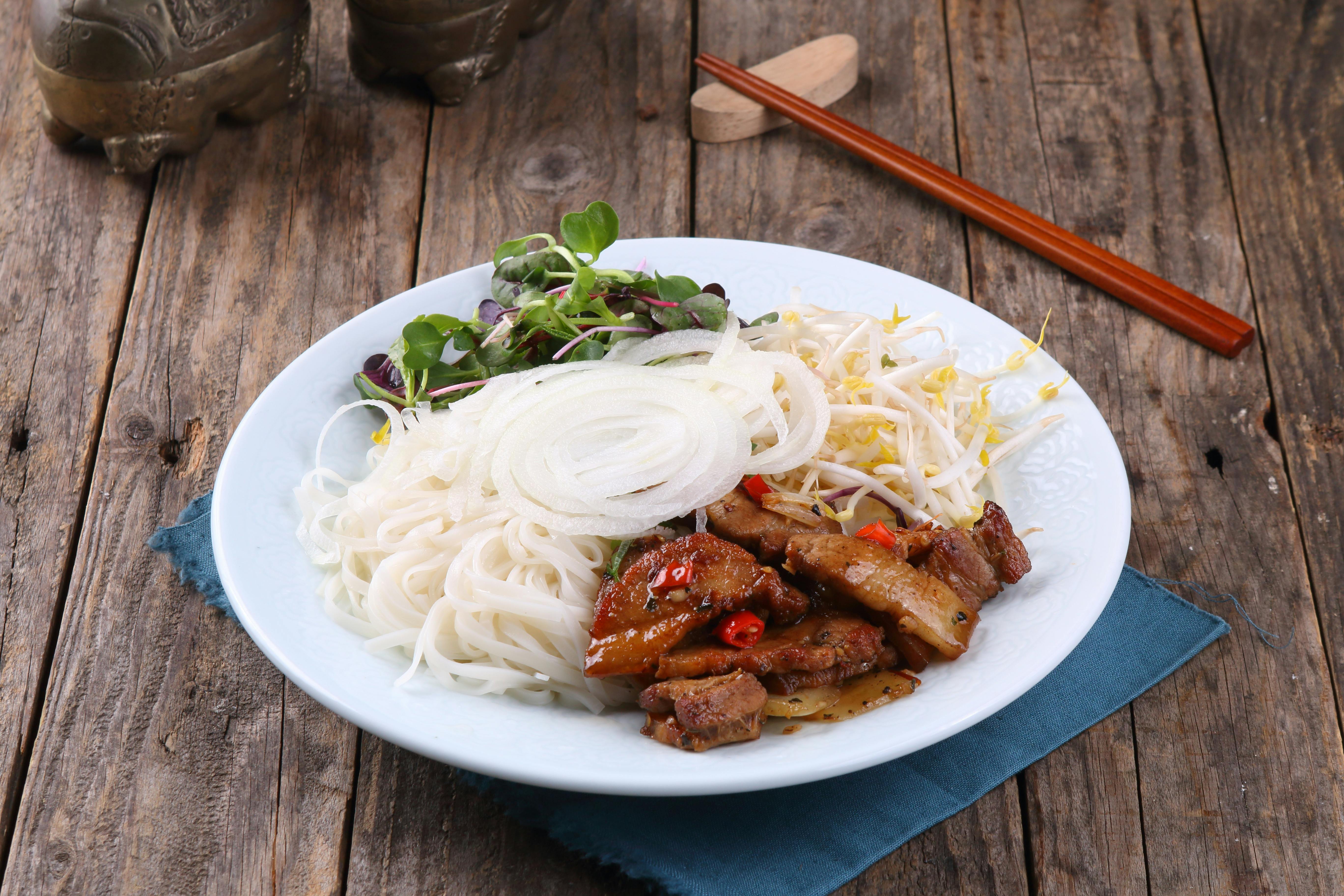 Traditional Vietnamese dish of grilled pork, rice noodles, and fresh vegetables served on a rustic wooden table.