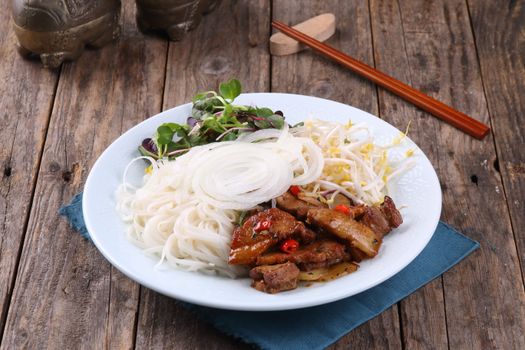 Traditional Vietnamese dish of grilled pork, rice noodles, and fresh vegetables served on a rustic wooden table.