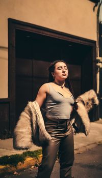 A young woman exudes confidence in a city setting, wearing a fur coat with attitude.