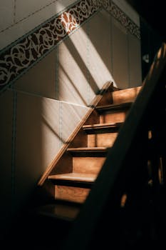 Wooden staircase illuminated by sunlight, highlighting ornate wall details and creating dramatic shadows.