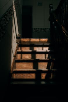 A moody staircase with intricate woodwork, illuminated by soft natural light casting dramatic shadows.
