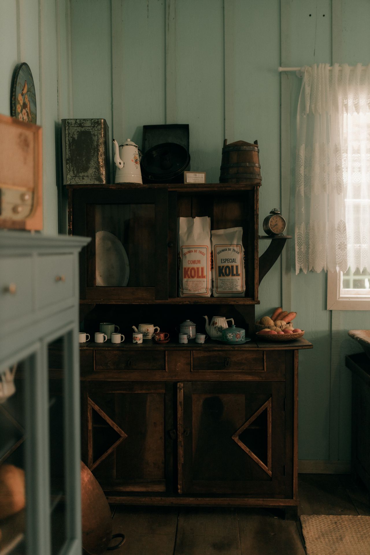 Rustic wooden hutch with glass doors holding vintage kitchenware against a beadboard wall