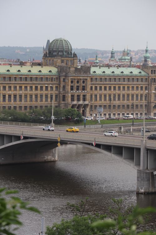 Free View of a historic building by a river in Prague with a bridge and vehicles. Stock Photo
