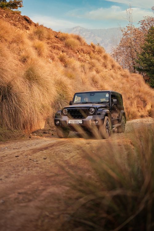 Free Black SUV navigating a rugged mountain trail with grassy terrain. Stock Photo