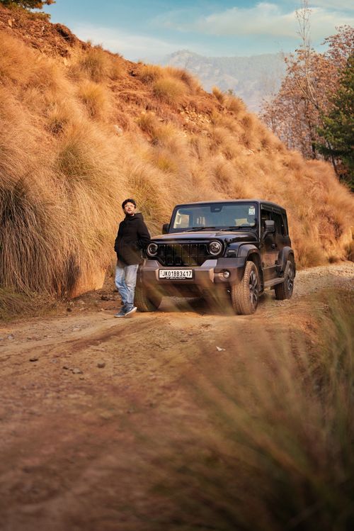 Free A person stands beside a black Jeep on a dirt road, surrounded by dry grass and hills. Stock Photo