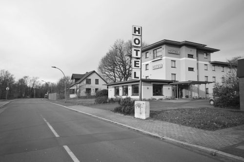 Free Black and white image of a suburban hotel with a prominent sign and empty street. Stock Photo