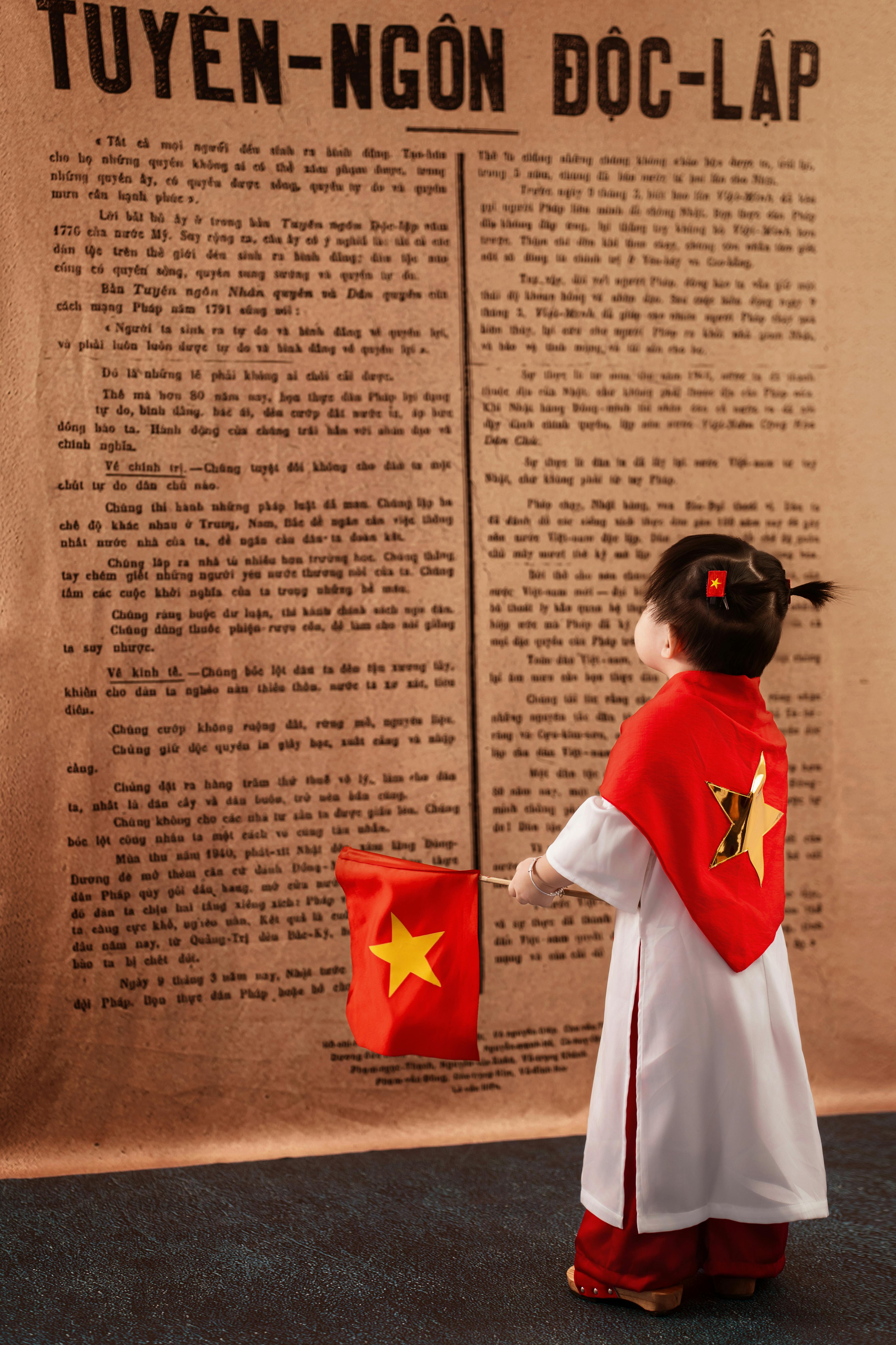 Young child in traditional Vietnamese dress celebrating with flag in Ho Chi Minh City.
