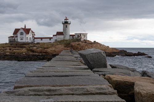 Free A picturesque lighthouse on rocky coastline under overcast sky in Gloucester, Massachusetts. Stock Photo
