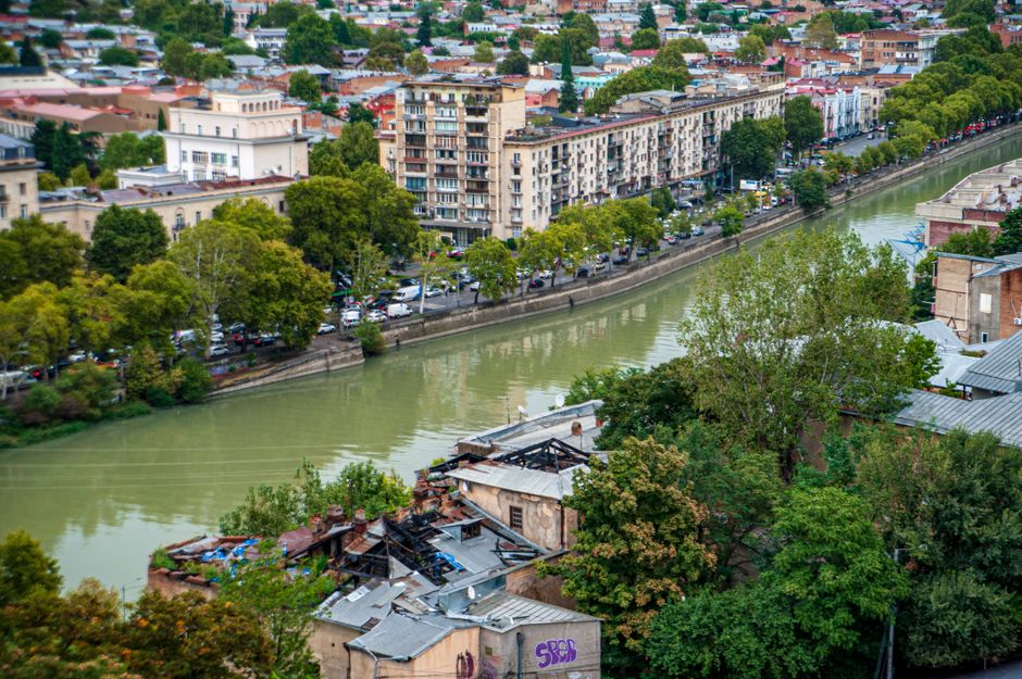 Aerial view of city buildings lining a river surrounded by lush trees and urban scenery. Aerial view of city buildings lining a river surrounded by lush trees and urban scenery.