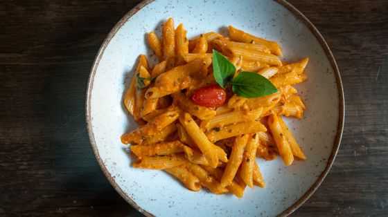 Penne in pink-orange tomato cream sauce with cherry tomato and basil leaves
