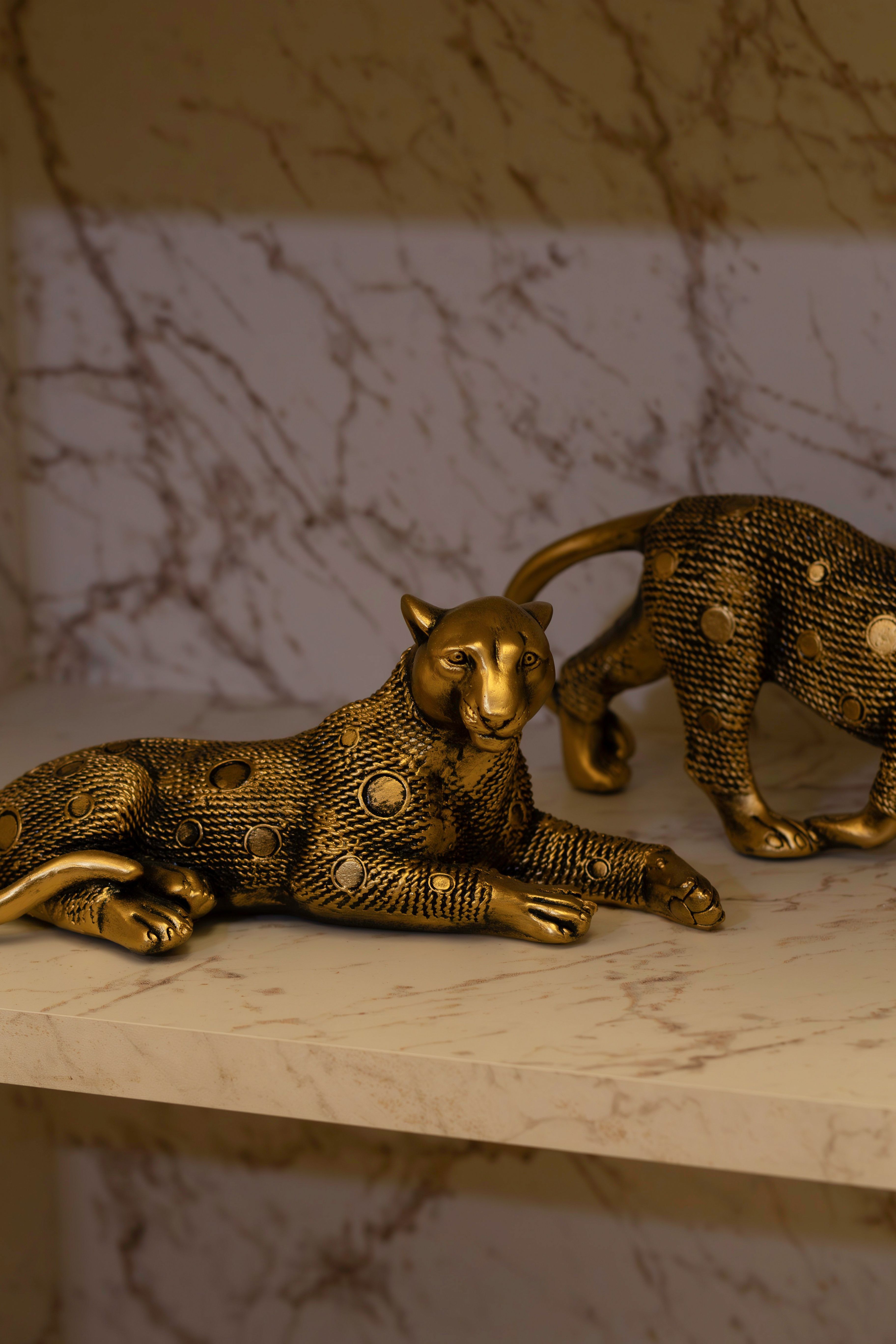 Two intricate golden panther sculptures on a marble shelf, exuding luxury and artistic craftsmanship.