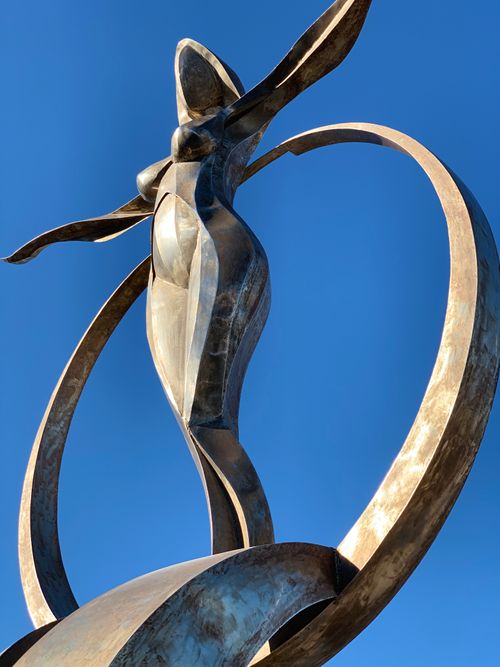 Free Dynamic sculpture of a woman reaching into the sky against a clear blue background. Stock Photo