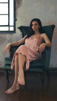 Woman in pink dress lounging in vintage chair, natural light indoors.