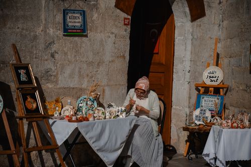 Free An elderly artisan crafting pottery at a traditional market stall with handmade ceramics on display. Stock Photo