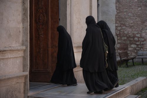 Free Three women in black hijabs enter a historical stone building through a wooden door. Stock Photo