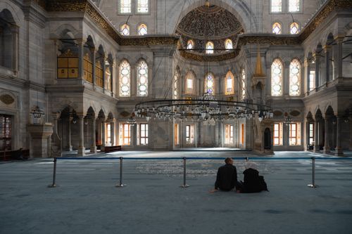 Free Two people sit inside an ornate, historic mosque, showcasing intricate architecture. Stock Photo