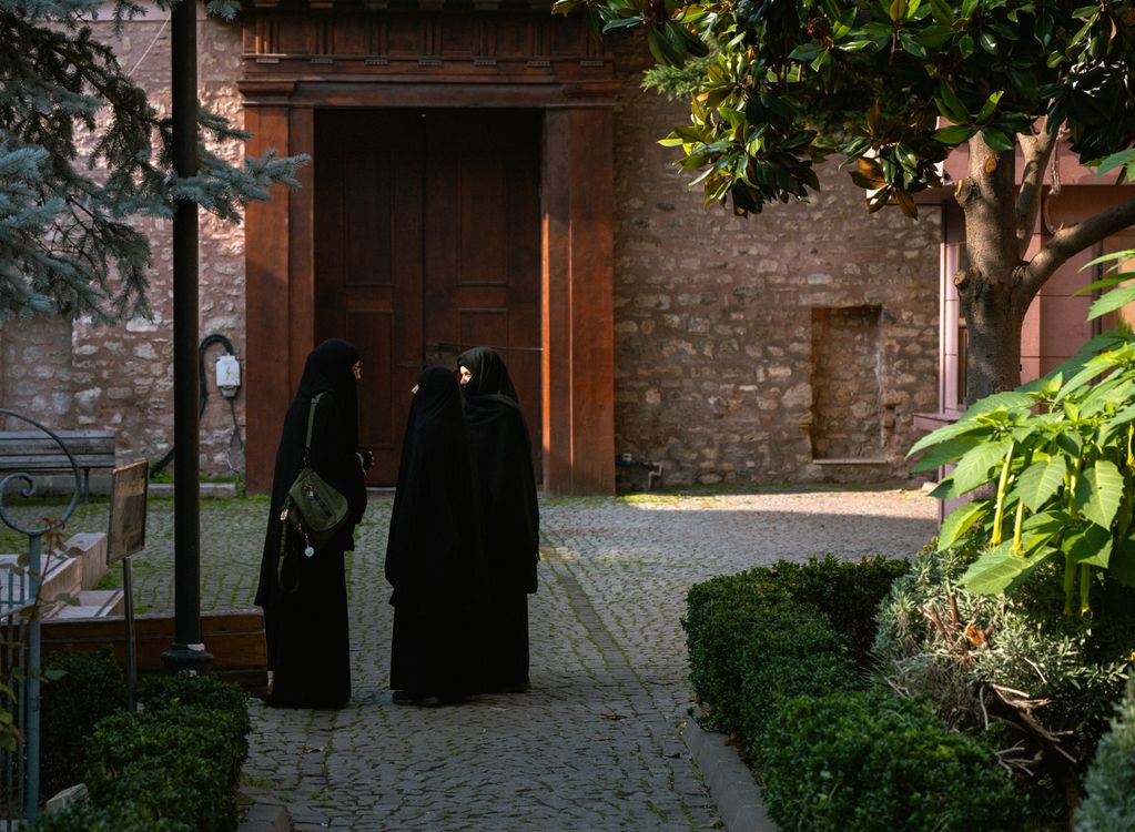 Free Three women in black hijabs conversing in a peaceful, historic courtyard. Stock Photo