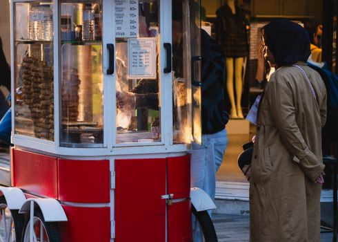 A woman stands at a street vendor cart buying pretzels at twilight, creating a warm, bustling atmosphere.