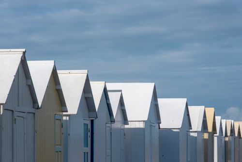 Free Row of colorful beach huts with white roofs under a clear blue sky, creating a serene coastal scene. Stock Photo