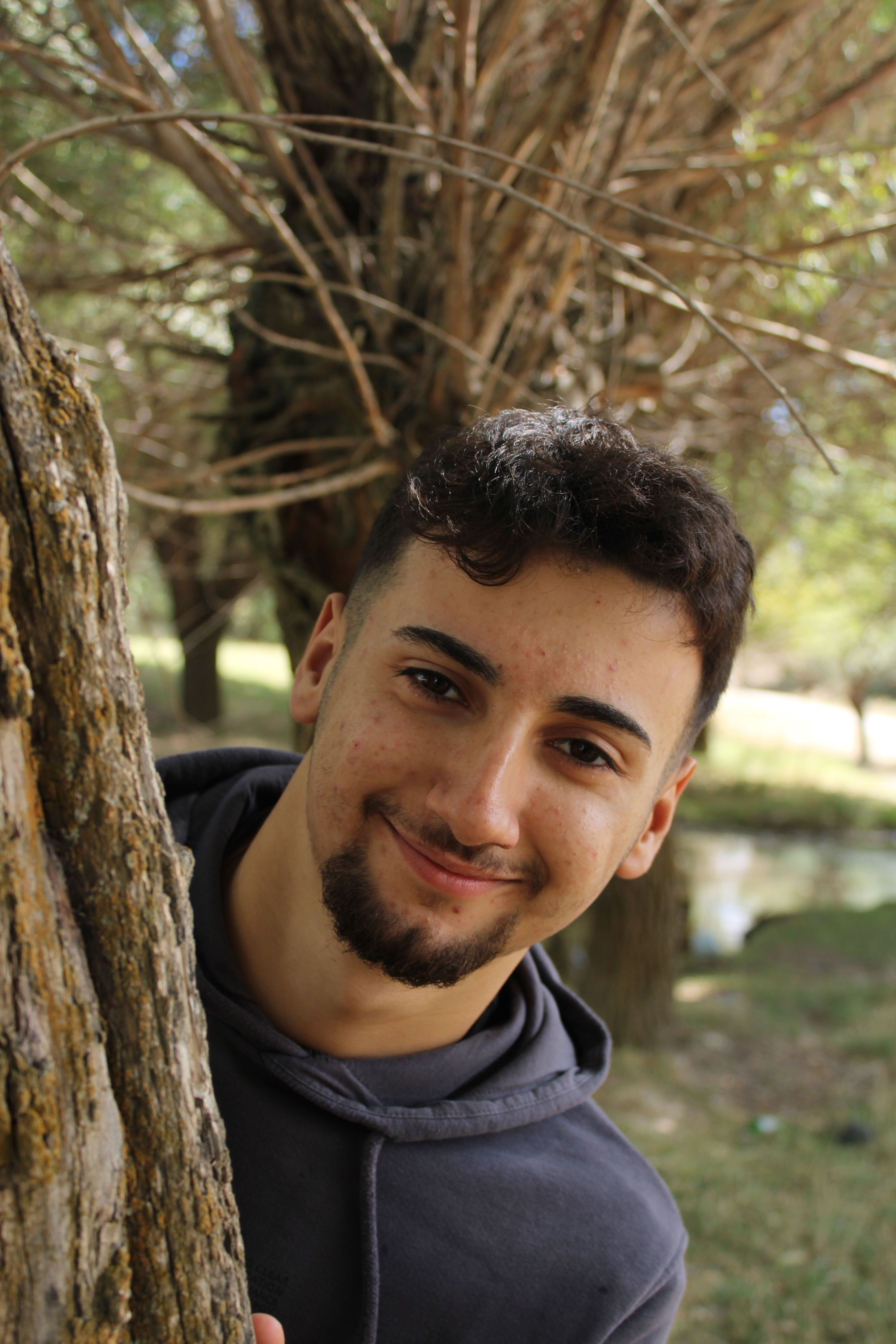 Portrait of a smiling young man peeking from behind a tree in a park in Nevşehir, Türkiye.