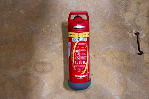 Red Isogard fire extinguisher mounted on a textured wall, focused view.