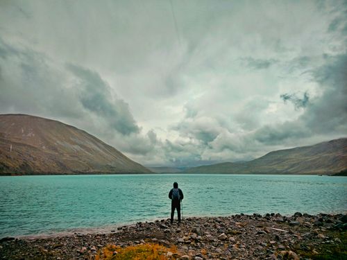 Free A lone hiker stands by a peaceful lake in Cuzco, Peru, surrounded by dramatic mountains. Stock Photo