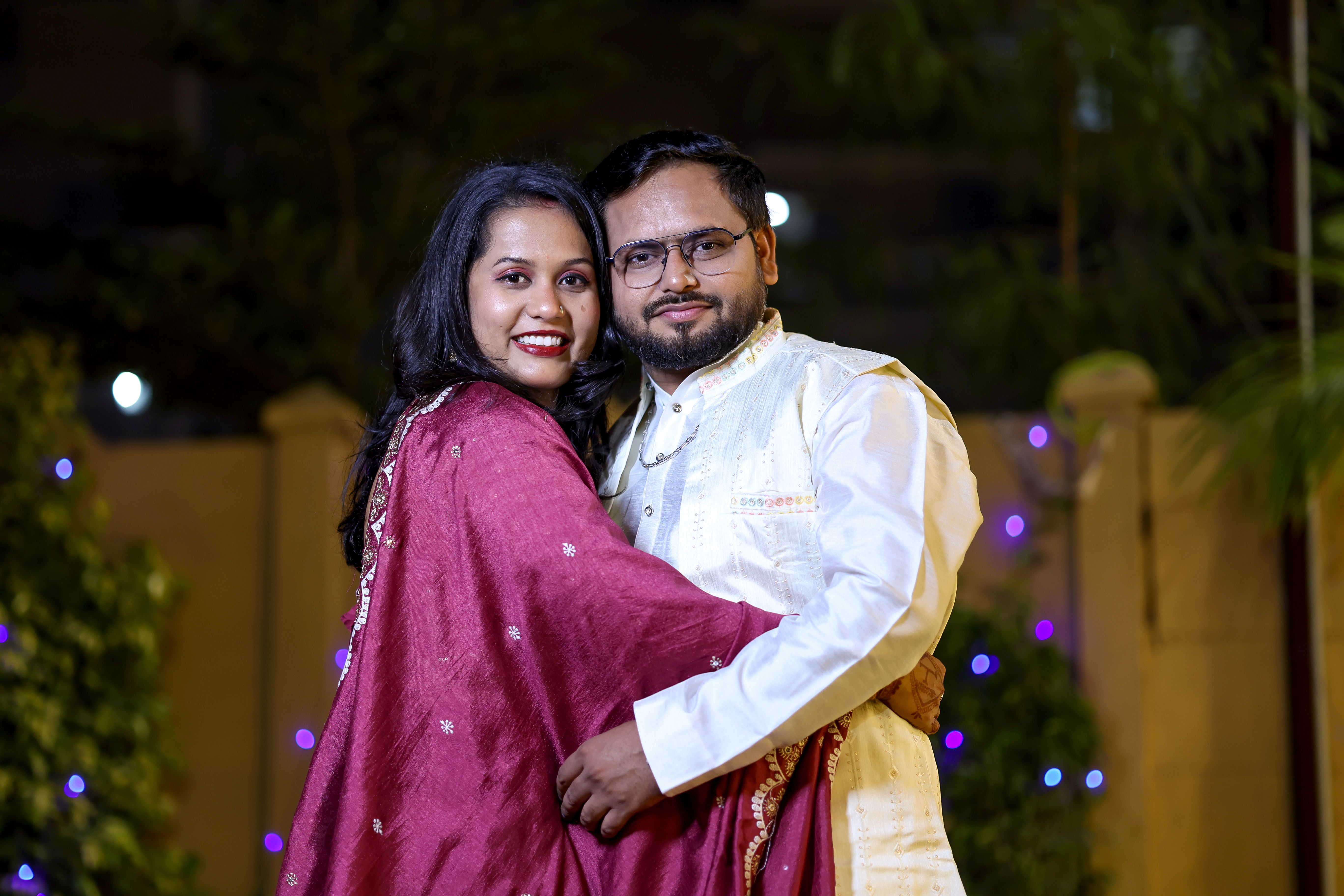 A joyful couple embracing outdoors at night, illuminated with festive lights.