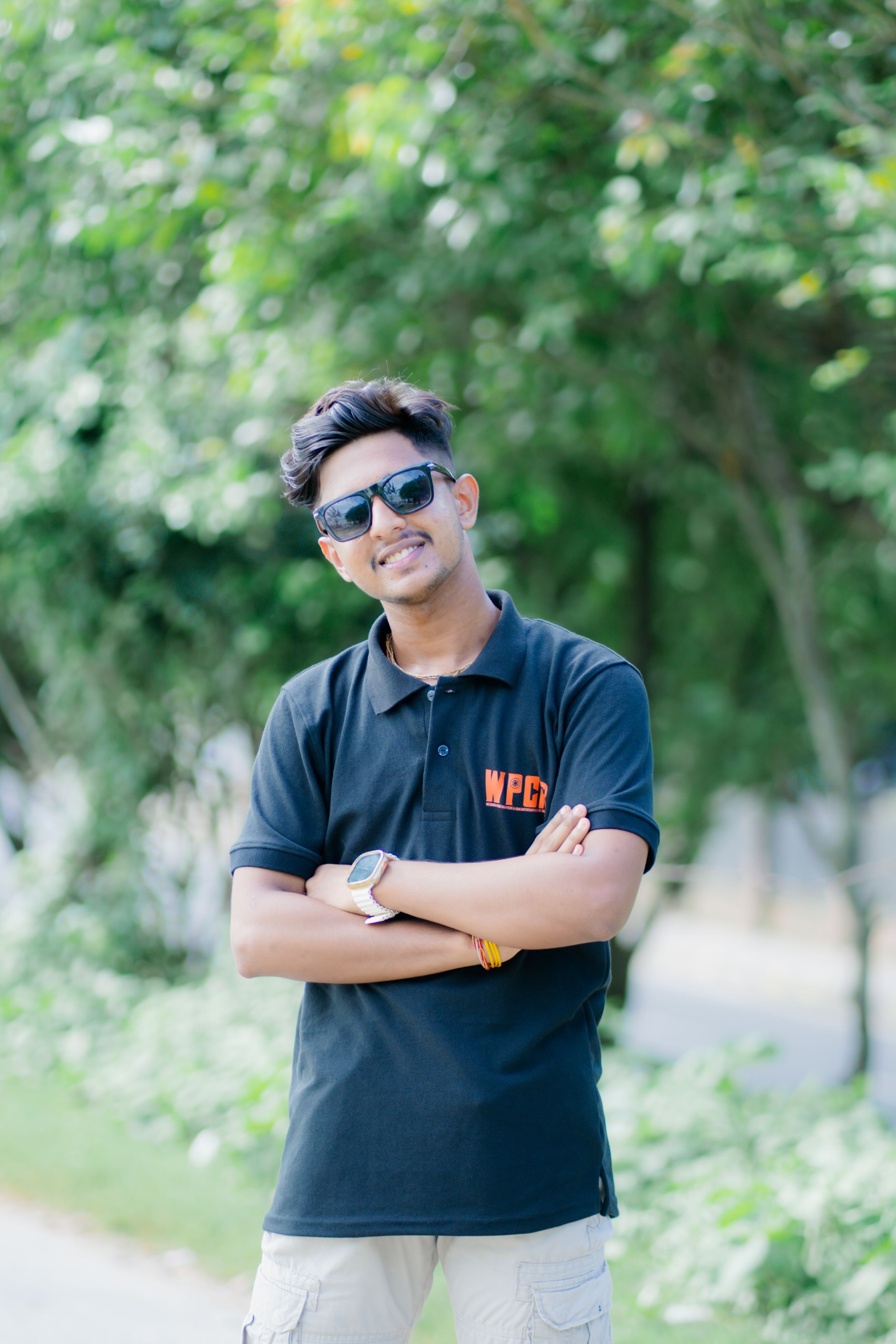 Smiling young man wearing sunglasses and a black polo shirt, enjoying a sunny day outdoors.