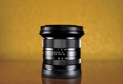 Close-up of a black camera lens on a reflective surface with yellow background.