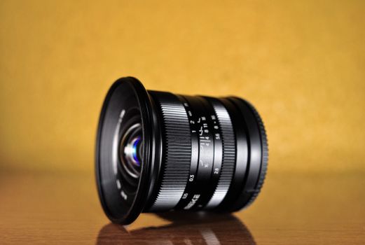 Detailed photo of a camera lens with focus settings against a warm yellow background.