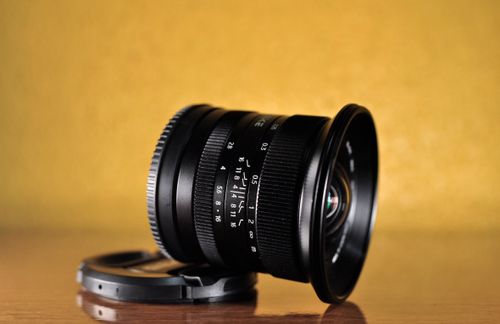 Free Close-up of a black camera lens placed on a wooden surface with a yellow background. Stock Photo