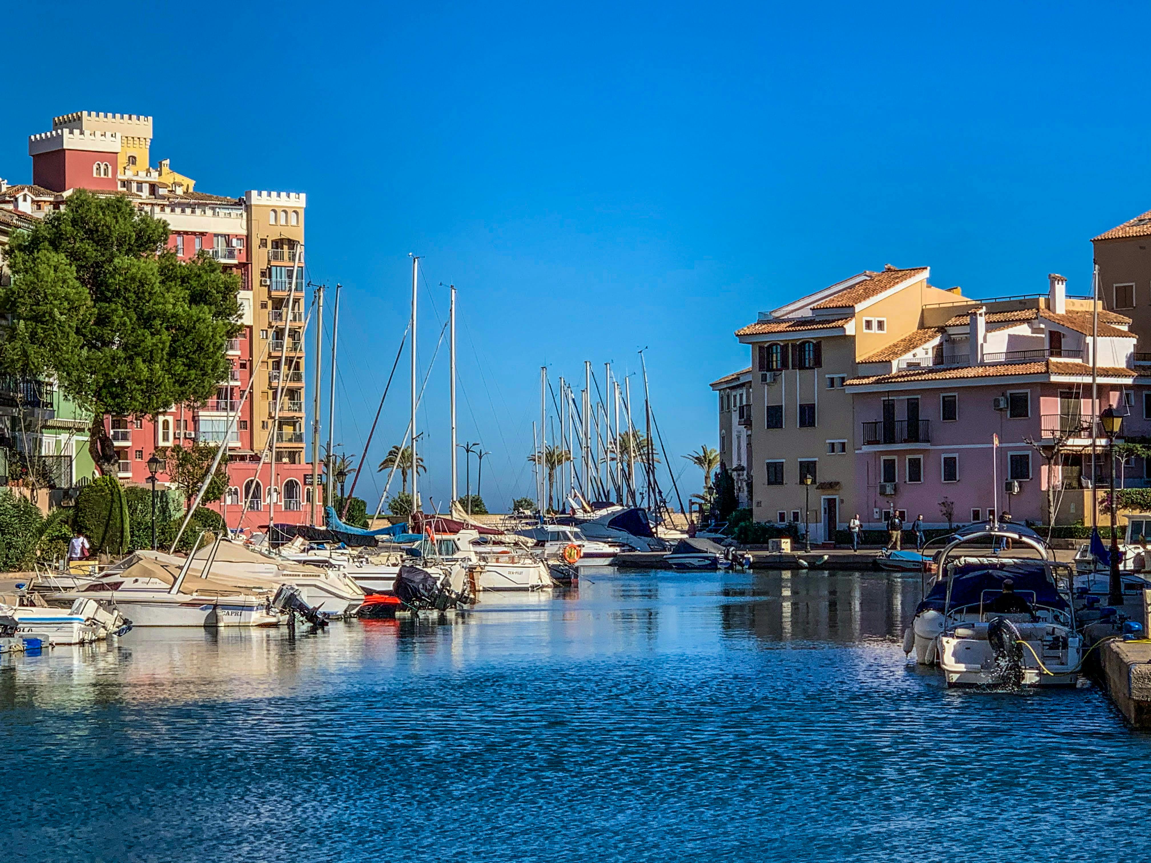 Vibrant marina scene with yachts docked along colorful Mediterranean-style buildings under a clear blue sky.